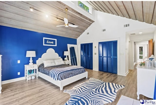bedroom featuring ceiling fan, high vaulted ceiling, wooden ceiling, multiple closets, and light wood-type flooring