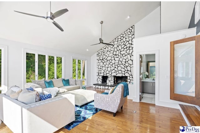 living room featuring high vaulted ceiling, a fireplace, ceiling fan, and light hardwood / wood-style flooring