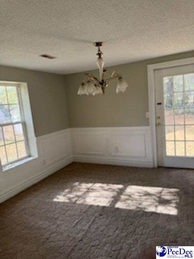 unfurnished dining area with an inviting chandelier, carpet flooring, and a textured ceiling