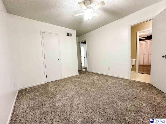 unfurnished bedroom featuring ceiling fan, carpet floors, ensuite bathroom, and a textured ceiling