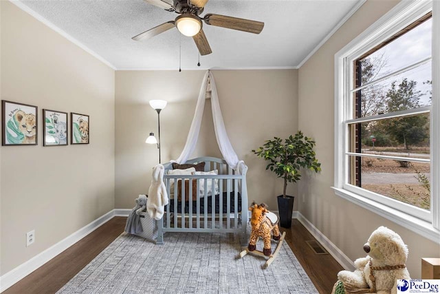 bedroom with crown molding, a textured ceiling, dark hardwood / wood-style floors, ceiling fan, and a crib