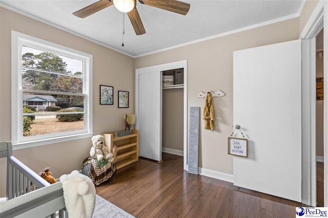 bedroom with crown molding, a crib, ceiling fan, dark hardwood / wood-style floors, and a closet