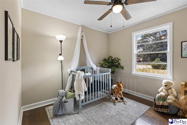 bedroom with a nursery area, hardwood / wood-style floors, ceiling fan, crown molding, and a textured ceiling