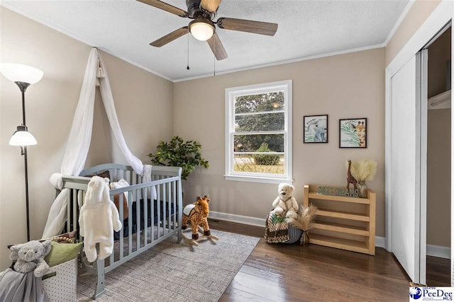 bedroom with ceiling fan, a crib, crown molding, dark wood-type flooring, and a textured ceiling