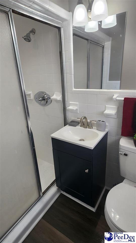 bathroom with tile walls, hardwood / wood-style flooring, vanity, an enclosed shower, and toilet