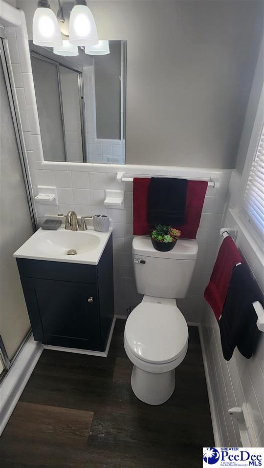 bathroom featuring tile walls, hardwood / wood-style floors, vanity, a shower with shower door, and toilet