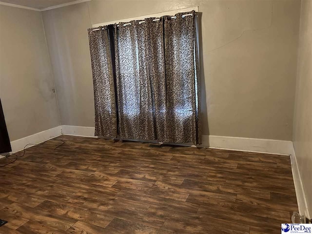 empty room featuring dark wood-type flooring and ornamental molding