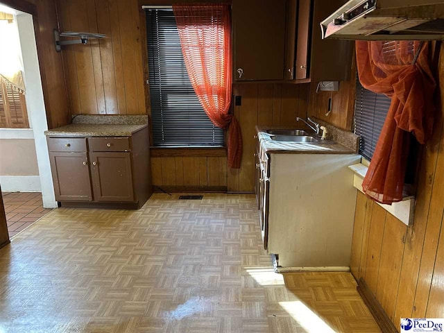 kitchen with dark brown cabinetry, light parquet flooring, sink, and wood walls