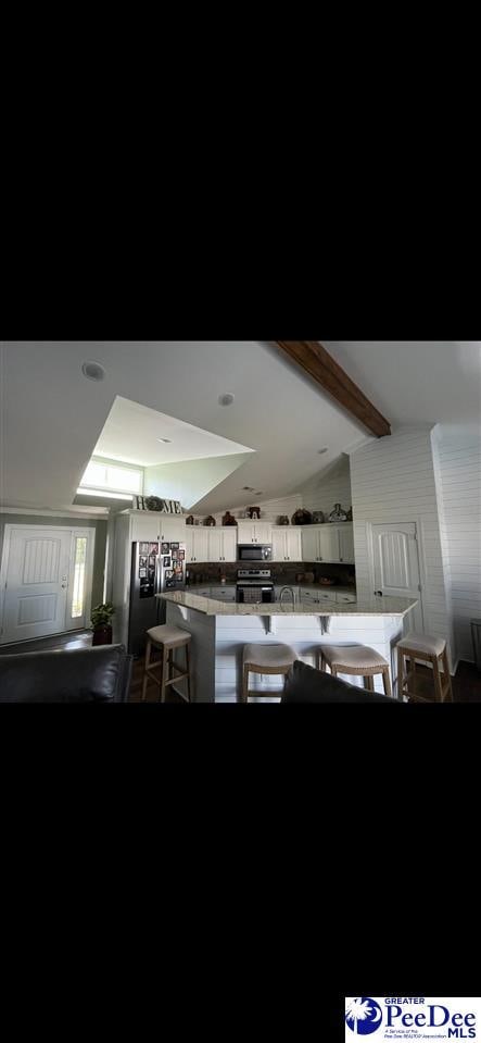 kitchen featuring appliances with stainless steel finishes, lofted ceiling with beams, white cabinetry, a kitchen bar, and kitchen peninsula