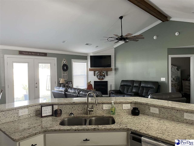 kitchen with sink, light stone counters, white cabinetry, lofted ceiling with beams, and a large fireplace