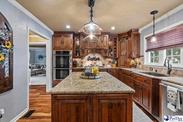 kitchen with a sink, appliances with stainless steel finishes, light wood finished floors, backsplash, and light stone countertops