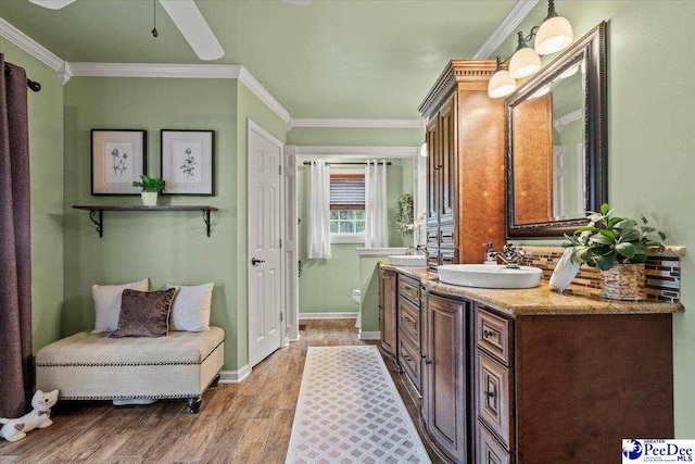 bathroom featuring wood finished floors, vanity, crown molding, baseboards, and toilet