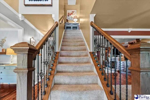 stairway with wood finished floors, baseboards, and ornamental molding