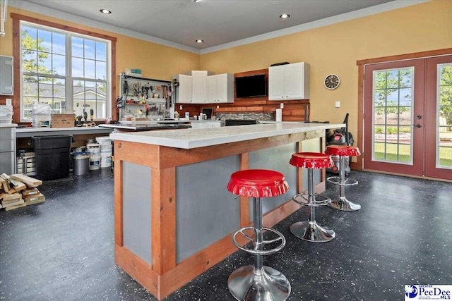 kitchen featuring healthy amount of natural light, white cabinetry, ornamental molding, light countertops, and a breakfast bar