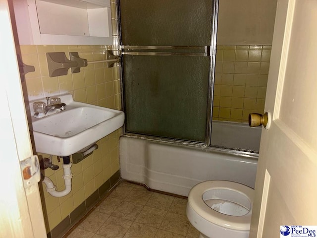 full bathroom with enclosed tub / shower combo, toilet, sink, and tile walls