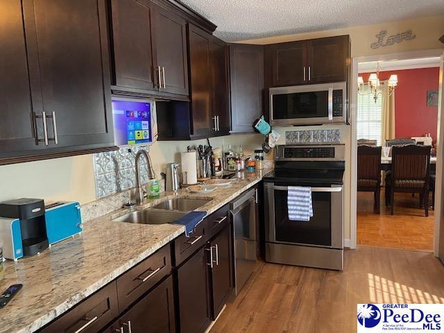 kitchen with appliances with stainless steel finishes, sink, dark brown cabinetry, light hardwood / wood-style floors, and a textured ceiling