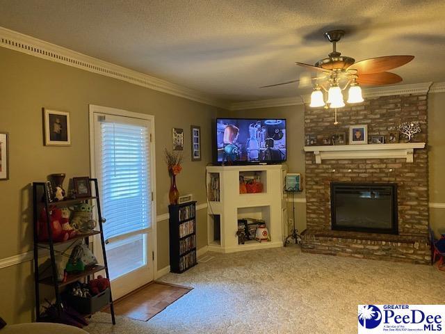 living room with crown molding, carpet floors, a brick fireplace, and a textured ceiling