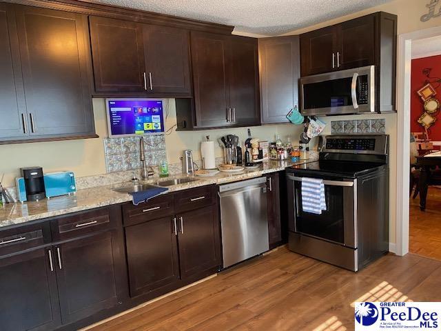 kitchen featuring dark brown cabinetry, sink, light wood-type flooring, appliances with stainless steel finishes, and light stone countertops