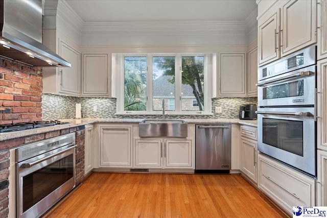 439 Whitman Ave, Florence, SC 29501 - kitchen featuring wall chimney exhaust hood, stainless steel appliances, light wood finished floors, backsplash, and crown molding