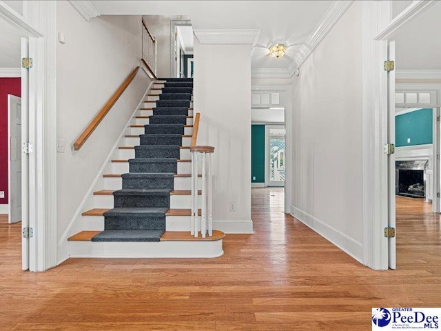 stairway with a high end fireplace, wood-type flooring, and ornamental molding