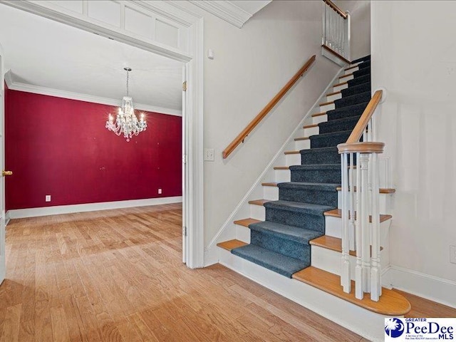 staircase featuring crown molding, wood-type flooring, and a chandelier