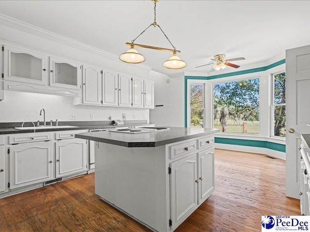 kitchen with sink, dark wood-type flooring, white cabinetry, ornamental molding, and a kitchen island