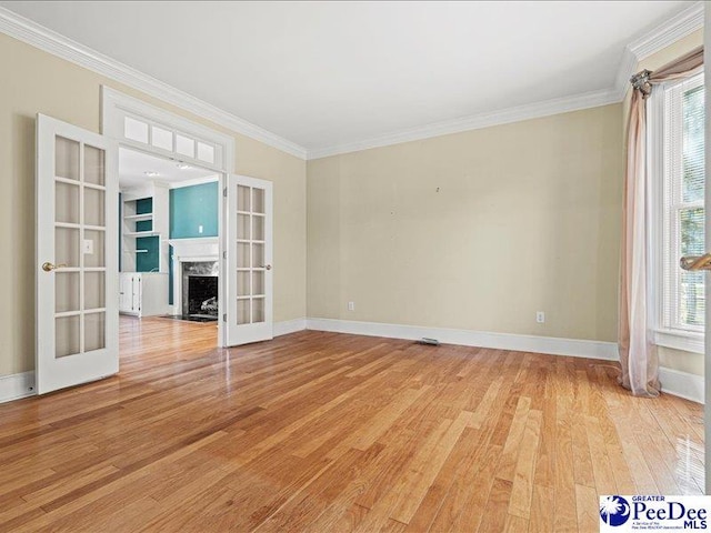 empty room with crown molding, a fireplace, light wood-type flooring, and french doors