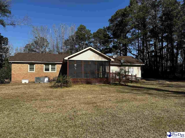 single story home with a front yard, a sunroom, brick siding, and central AC unit