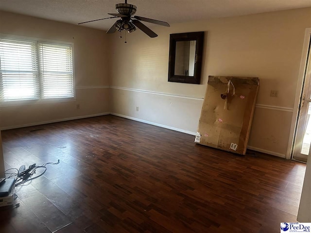 spare room featuring dark wood-style flooring, a ceiling fan, and baseboards