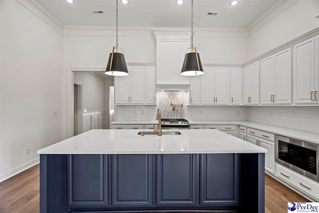 kitchen with pendant lighting, stainless steel microwave, light stone countertops, and an island with sink