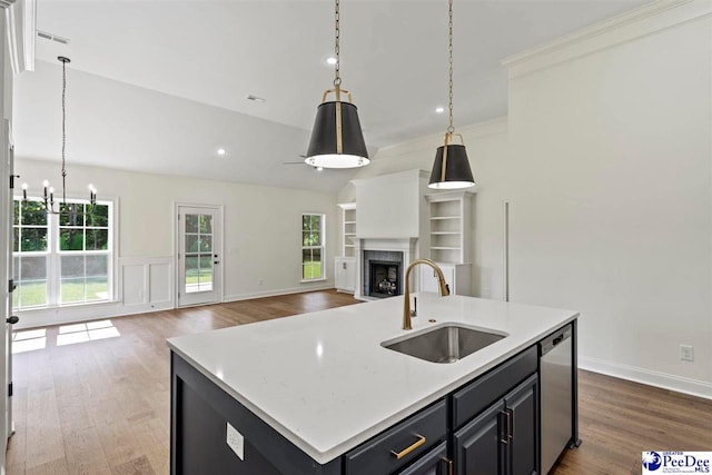 kitchen featuring dishwasher, wood-type flooring, sink, a high end fireplace, and a center island with sink