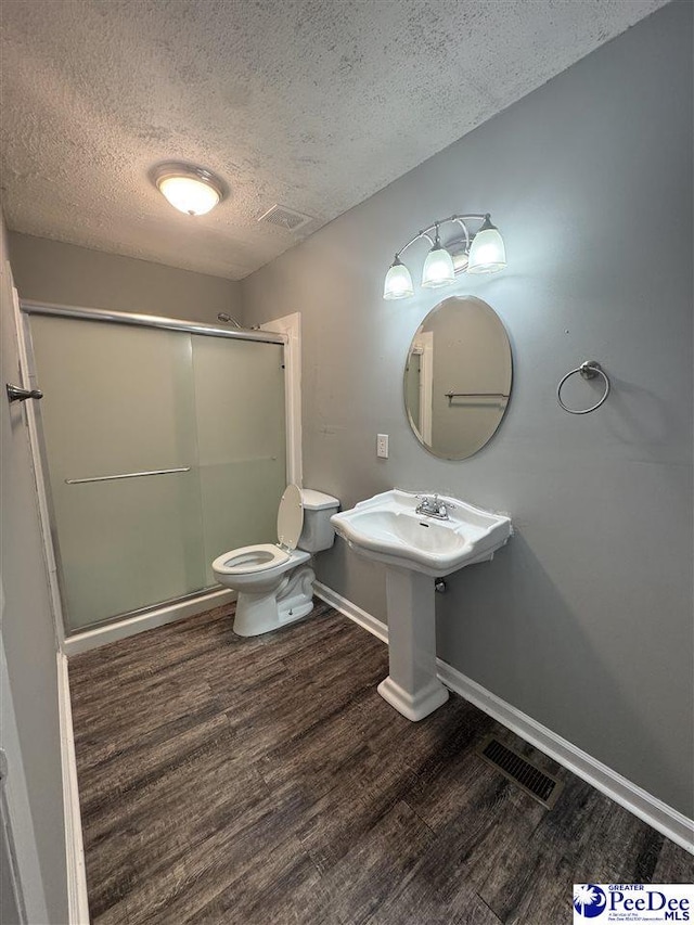 bathroom featuring hardwood / wood-style flooring, toilet, a textured ceiling, and a shower with shower door