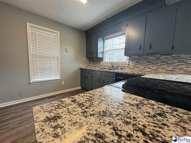 kitchen featuring sink, dark hardwood / wood-style floors, tasteful backsplash, light stone counters, and a textured ceiling