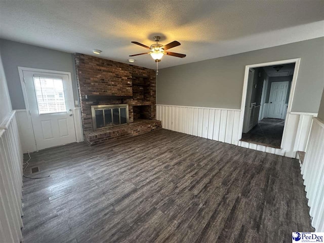 unfurnished living room with a brick fireplace, dark wood-type flooring, a textured ceiling, and ceiling fan