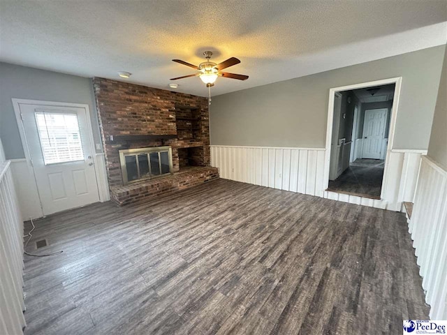 unfurnished living room featuring a brick fireplace, hardwood / wood-style flooring, a textured ceiling, and ceiling fan