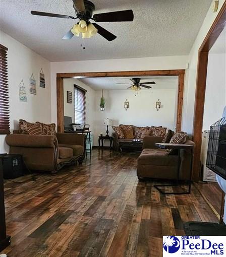 living room with ceiling fan, dark hardwood / wood-style floors, and a textured ceiling