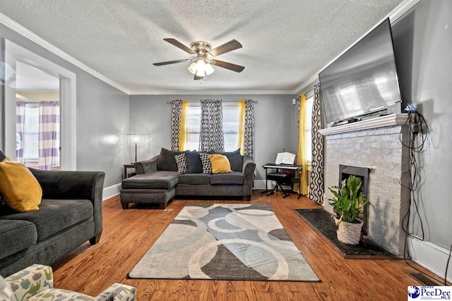 living room featuring crown molding, ceiling fan, a brick fireplace, and light wood-type flooring