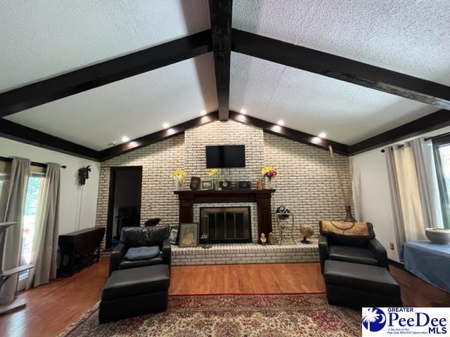 living room with a fireplace, dark wood-type flooring, lofted ceiling with beams, and a textured ceiling