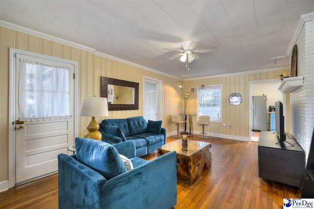 living area featuring a ceiling fan, crown molding, baseboards, and wood finished floors