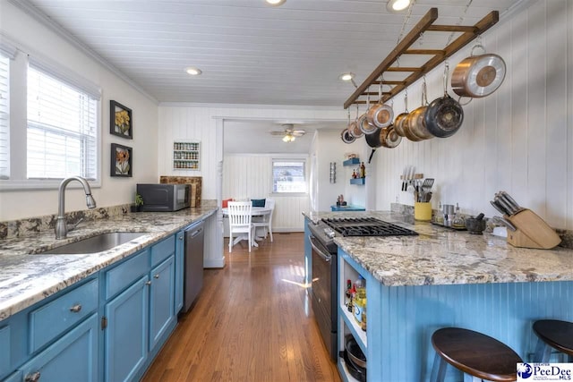 kitchen featuring dark wood-type flooring, blue cabinets, stainless steel appliances, a kitchen bar, and a sink