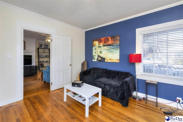 living area with a fireplace, crown molding, baseboards, and wood finished floors