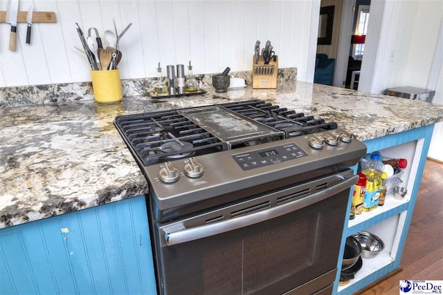 kitchen featuring blue cabinets, stone countertops, wood finished floors, and gas stove