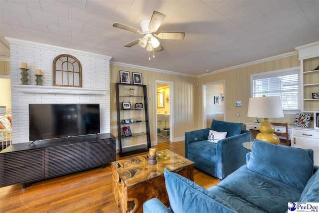 living room with a ceiling fan, a fireplace, ornamental molding, and wood finished floors