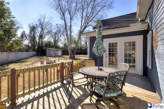 wooden terrace with a storage unit, outdoor dining area, an outdoor structure, and a fenced backyard