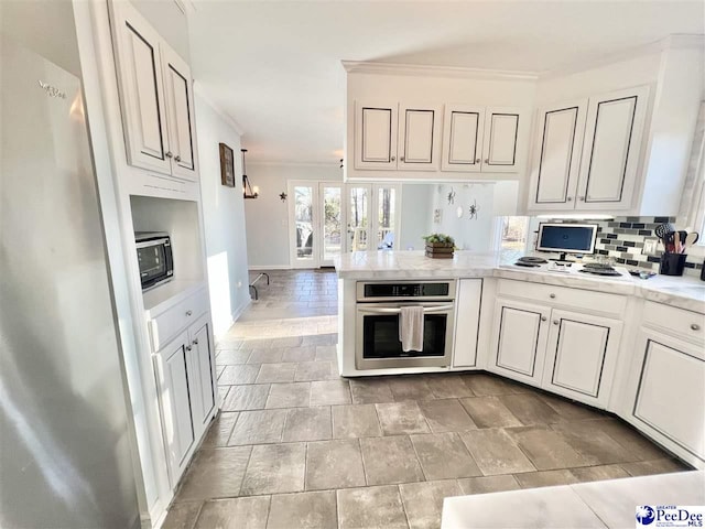 kitchen with ornamental molding, stainless steel appliances, a peninsula, light countertops, and decorative backsplash