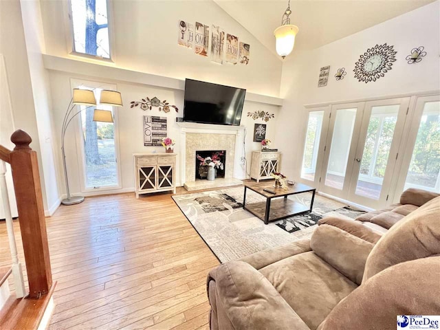 living area with high vaulted ceiling, hardwood / wood-style flooring, a high end fireplace, french doors, and baseboards