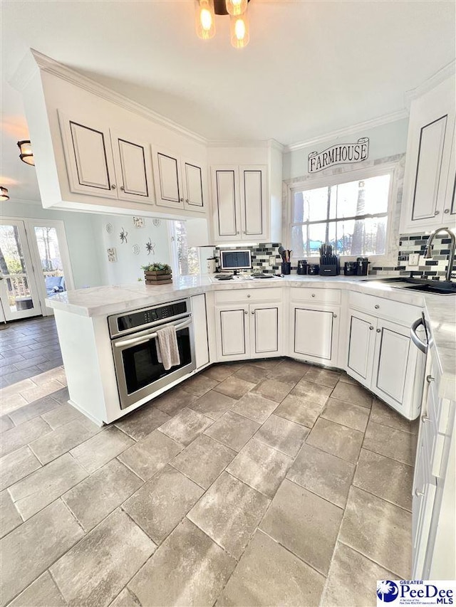 kitchen with stainless steel oven, decorative backsplash, a wealth of natural light, and a sink