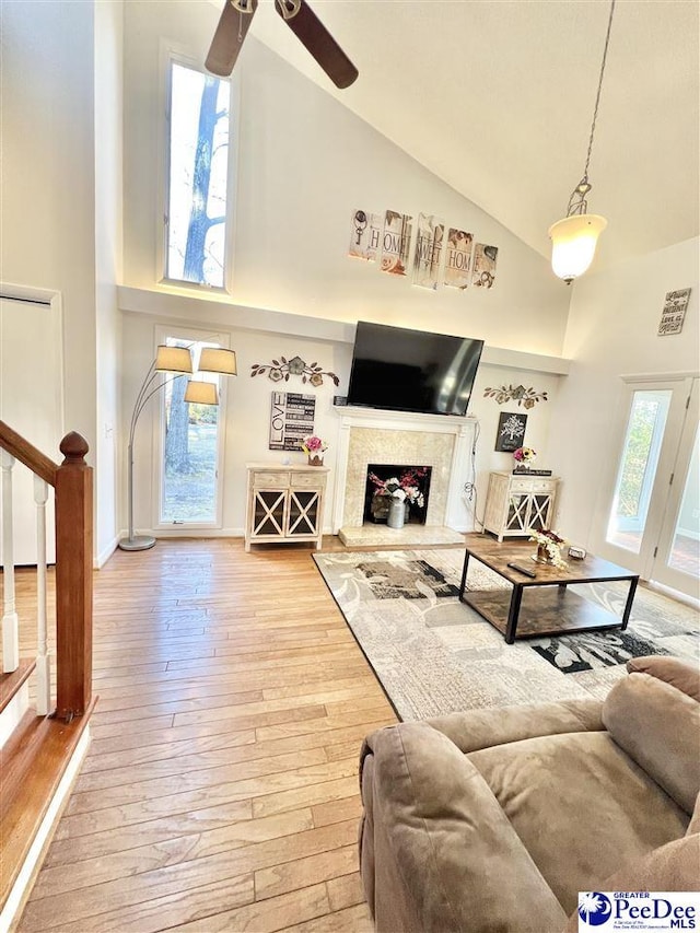 living room with high vaulted ceiling, a ceiling fan, hardwood / wood-style floors, stairway, and a fireplace