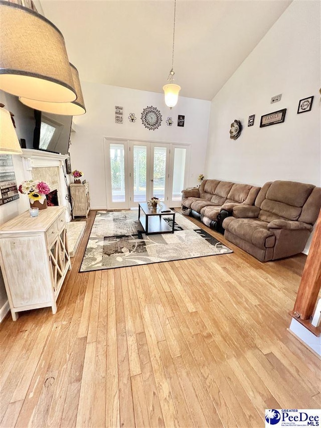 living room with light wood-type flooring, high vaulted ceiling, and french doors