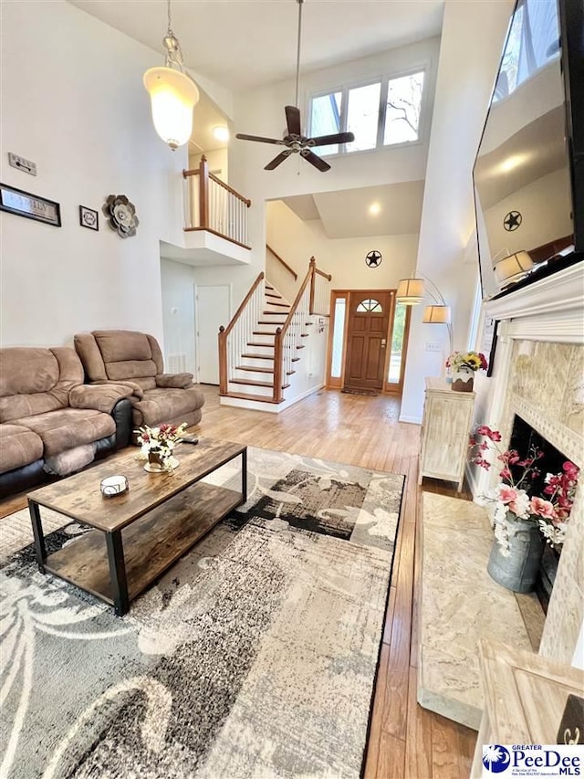 living room featuring stairs, light wood-style flooring, a towering ceiling, and a tile fireplace